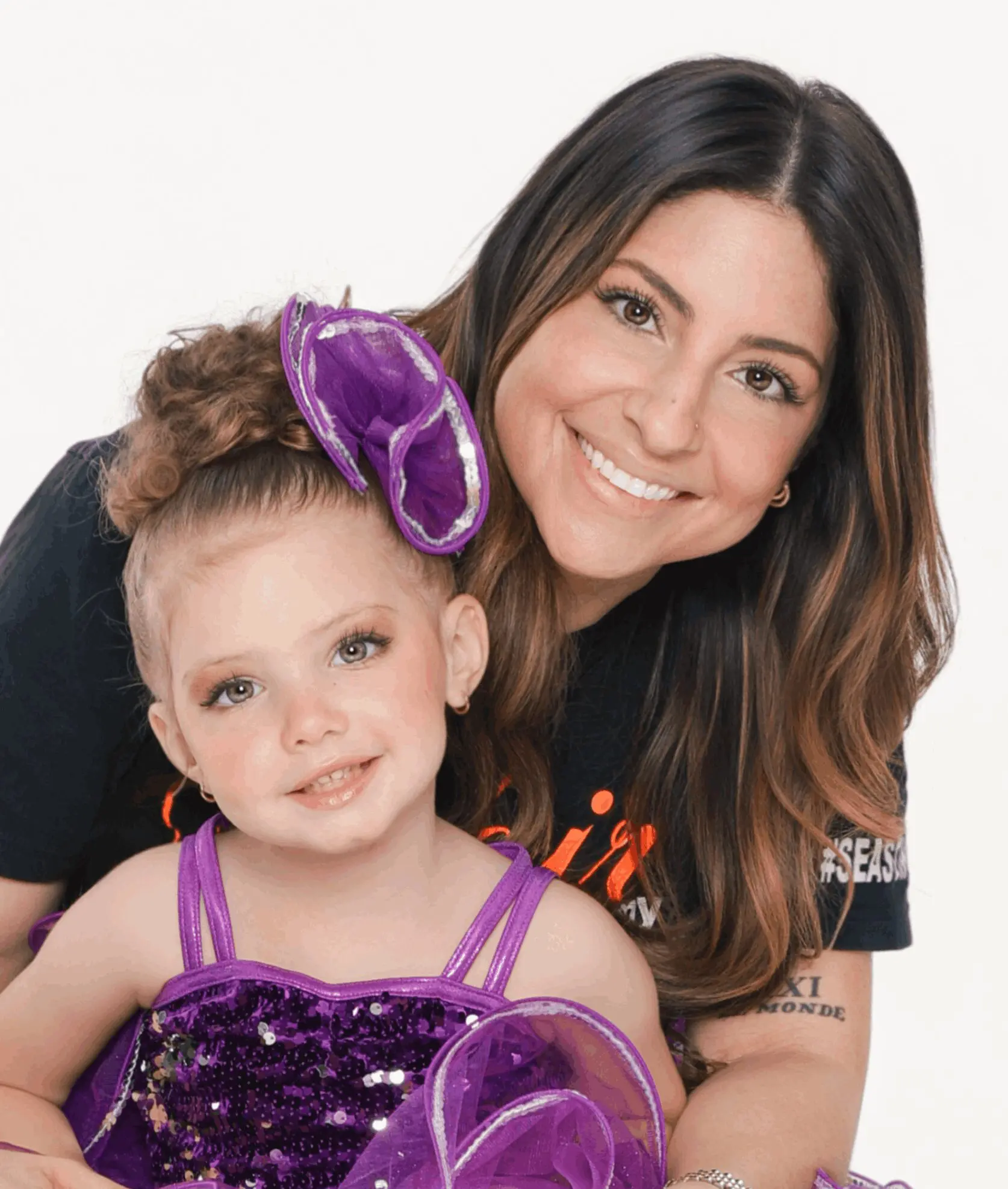A smiling woman with a young girl wearing a purple dress and headband.