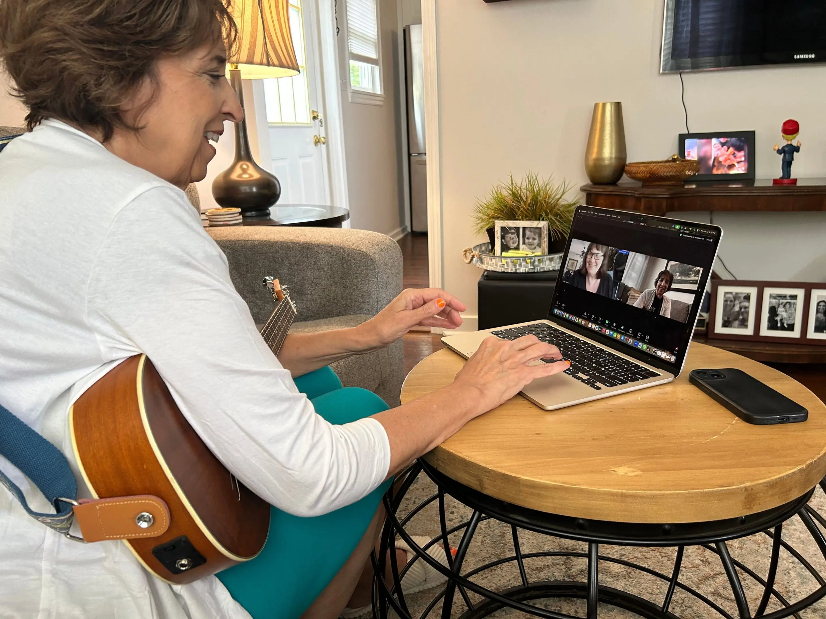 Woman playing guitar and video chatting on laptop at home.