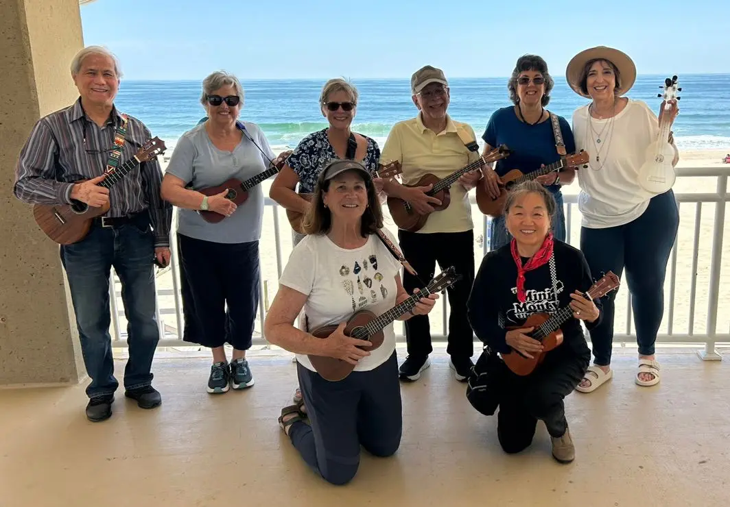 Group of people playing ukuleles together outdoors on a sunny day.