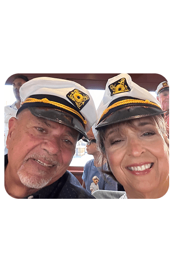 A smiling elderly couple wearing captain hats on a boat.